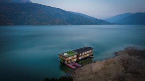 Une maison flottante, dotée d’une terrasse et d’un petit jardin, amarrée au bord d’un lac.