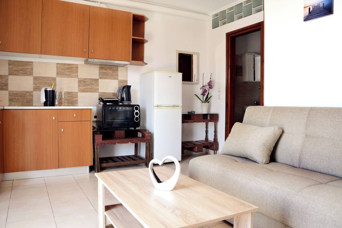 Un espace de vie compact comprenant un coin cuisine, un canapé, une table basse et un objet décoratif en forme de cœur.