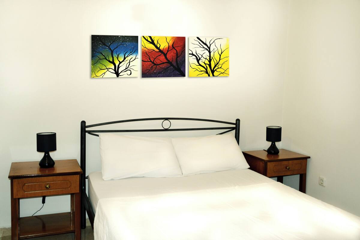 Une chambre à coucher comprenant un lit, deux tables de chevet et trois tableaux accrochés au mur.