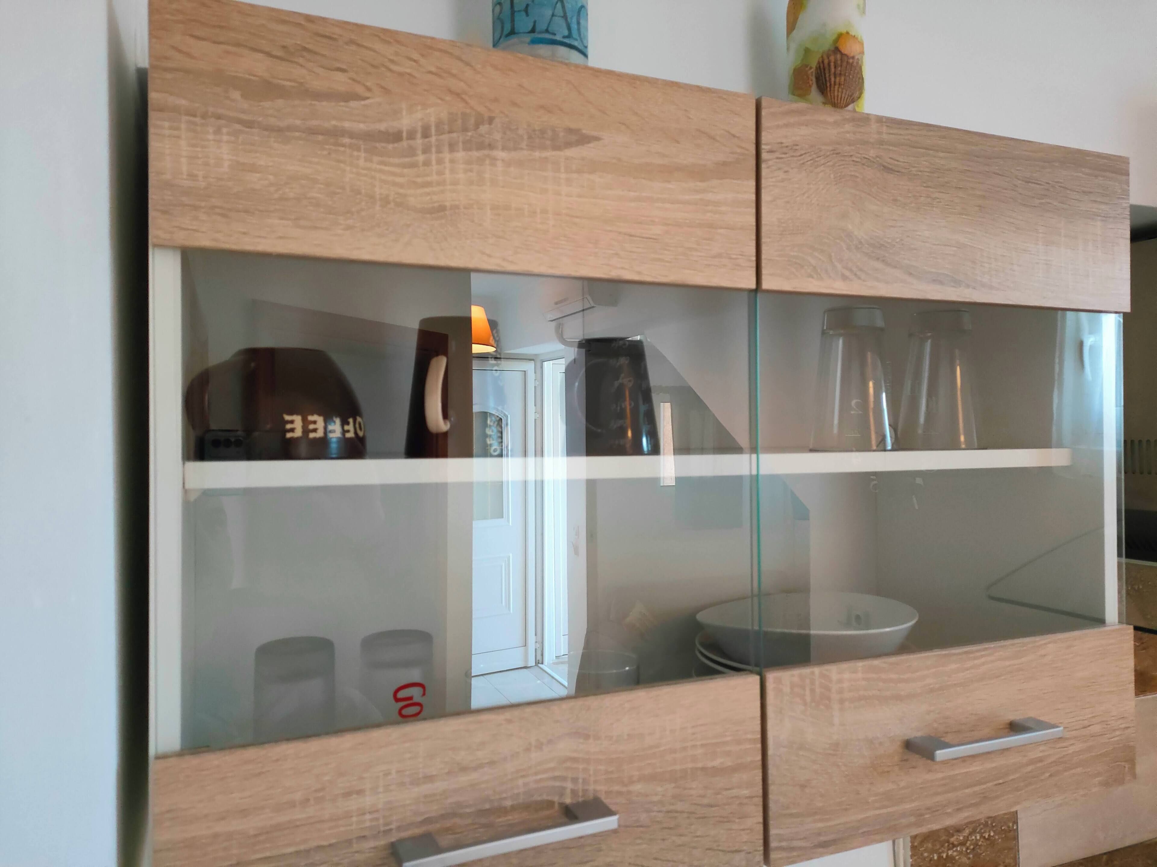 A wooden cabinet with glass doors containing kitchenware and a coffee maker.