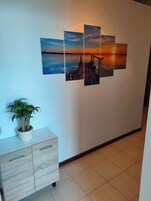 A hallway with a wall-mounted sunset painting, a potted plant, and a wooden cabinet.