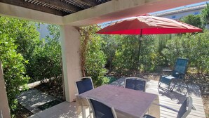 A covered patio with a table and chairs, a red umbrella, and a view of greenery. - Charming Villa 4 pers swimming pool terrace 600 m from the beach (Belgodère,)