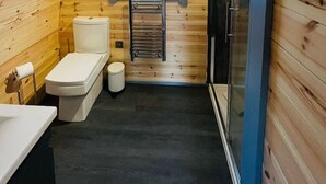 A compact wooden cabin bathroom with a window, a toilet, a sink, and a shower area.