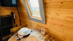 A wooden interior with a dining table set for two, a television mounted on the wall, and a window with a view.