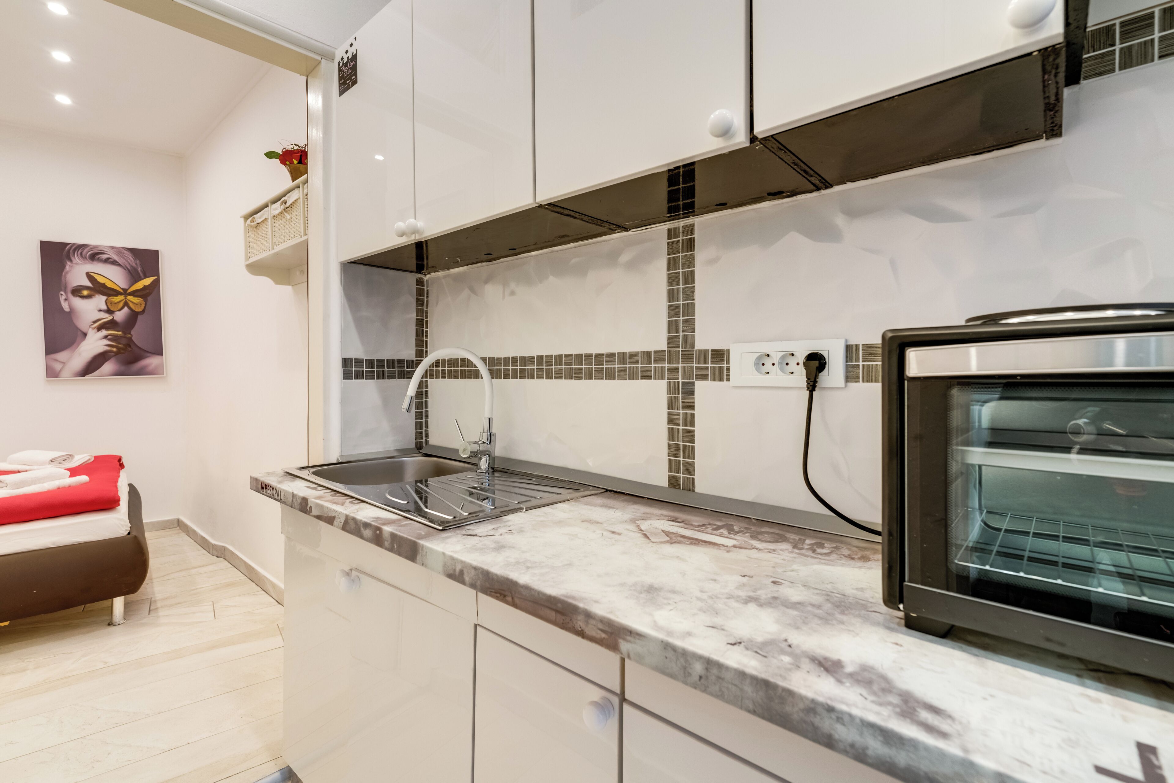 A modern kitchen with white cabinets, a marble countertop, a built-in oven, and a sink.