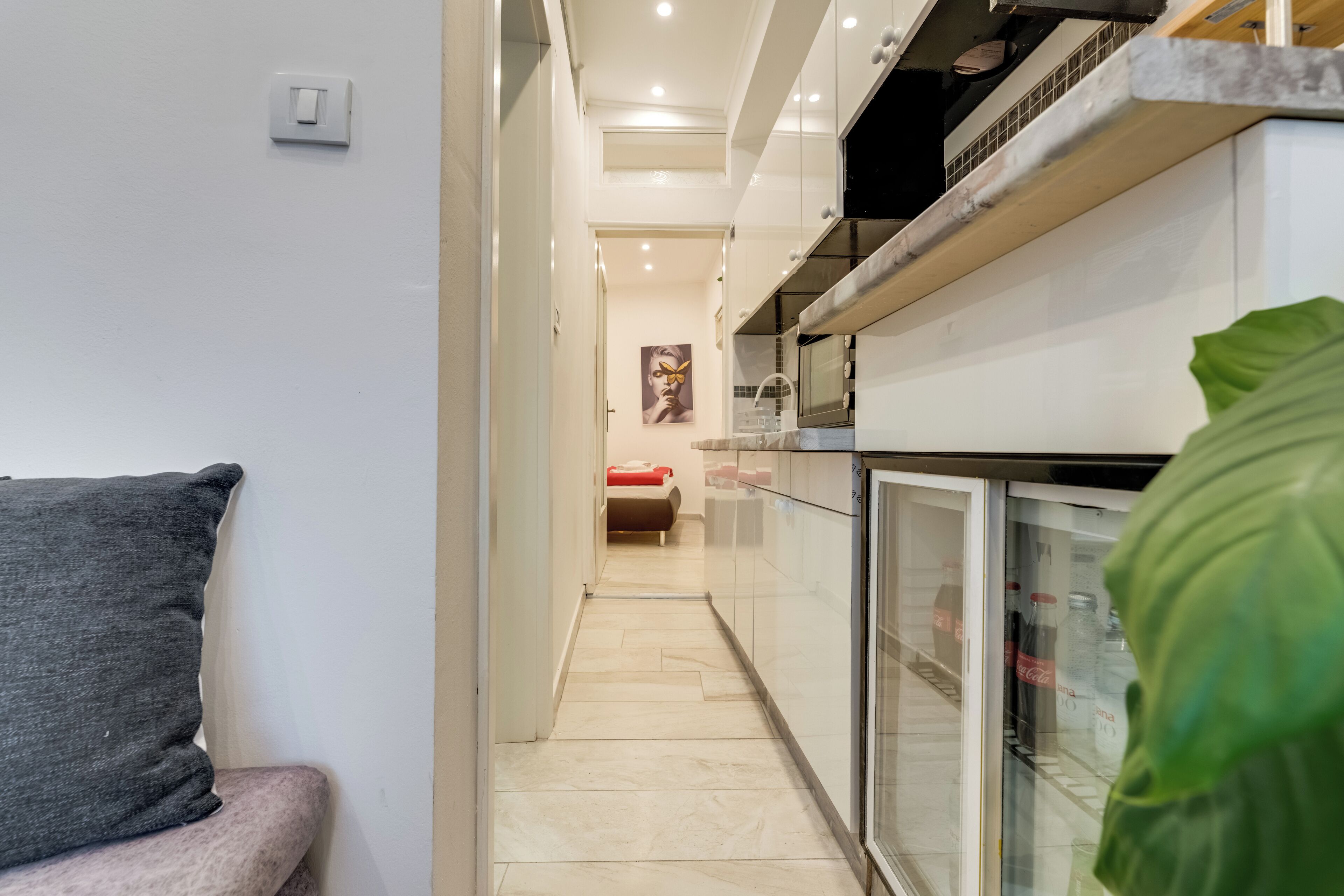 Una cocina moderna equipada con refrigerador, microondas y estufa. Un pasillo conduce a un dormitorio con una cama y un cuadro en la pared.