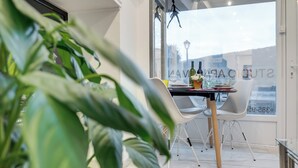 Ein stilvoller Essbereich mit einem Tisch f ür zwei Personen, einer Zimmerpflanze im Vordergrund und Blick auf die Stadt durch große Fenster.