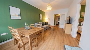 Ein Essbereich mit einem Holztisch und Stühlen, einer Couch und einem Fernseher in einem Zimmer mit grünen Wänden und Holzböden.