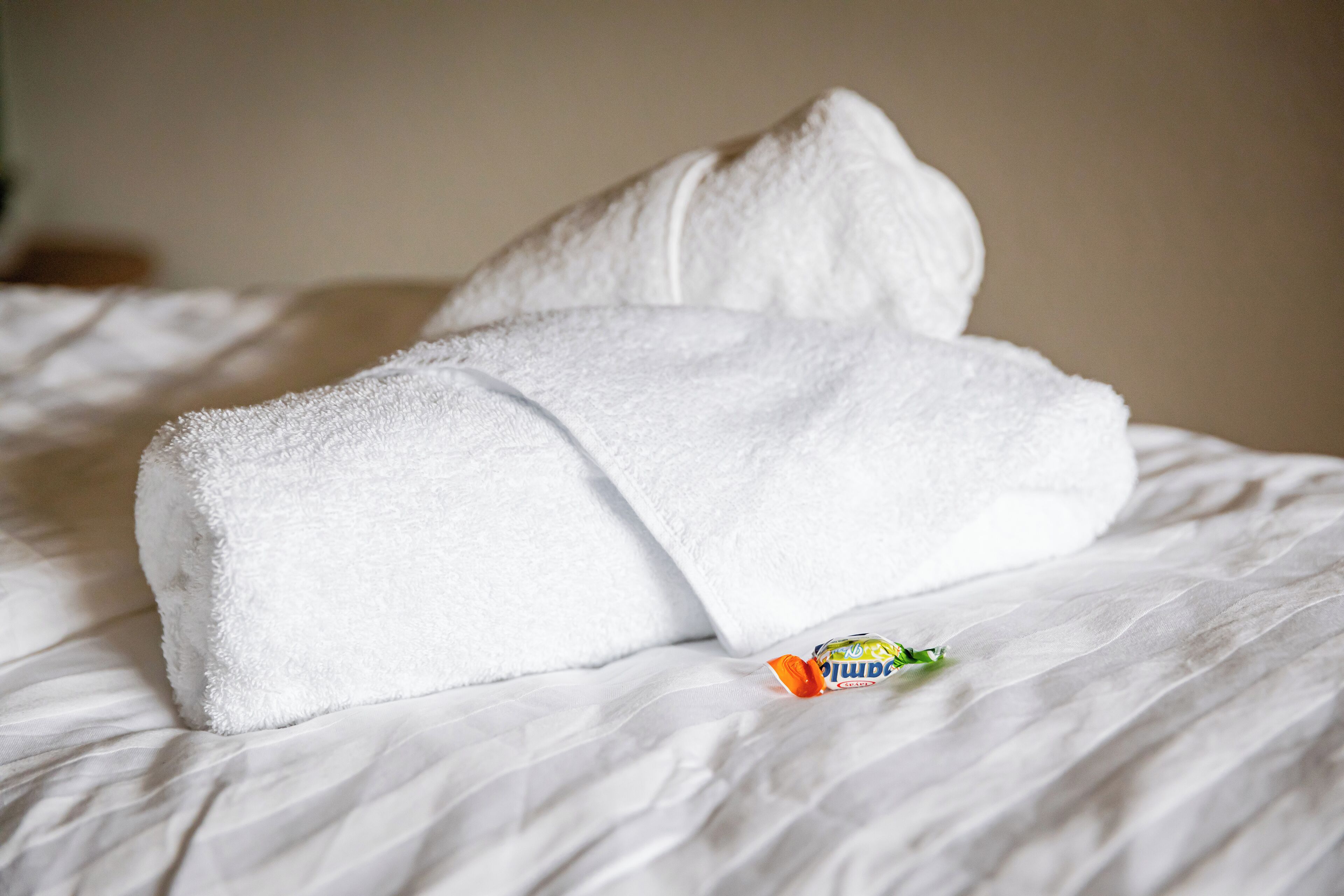 Un lit bien fait, avec une serviette blanche pliée et un petit flacon de lotion posé dessus.