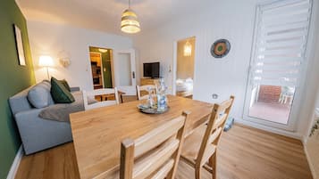 Ein Essbereich mit Holztisch und Stühlen, einer Couch, einem Fernseher und einer Deckenleuchte.