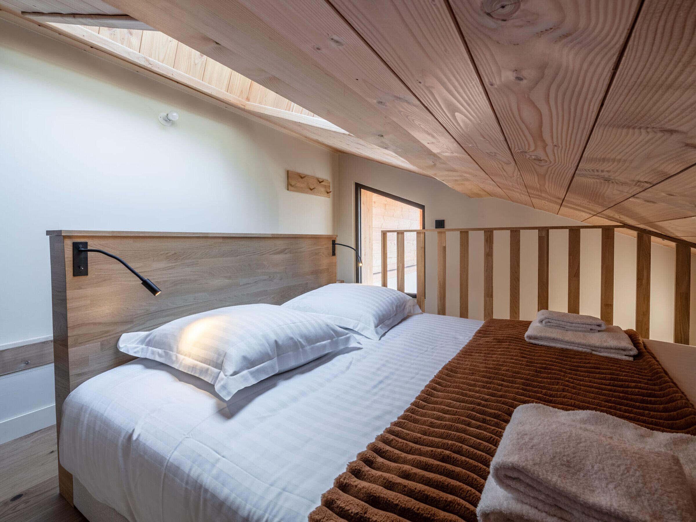 A bedroom with a wooden headboard, a bed with white bedding, a brown rug, and a window providing natural light.