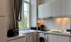 Une cuisine moderne avec des meubles blancs, une machine à café, un grille-pain et un lave-linge.