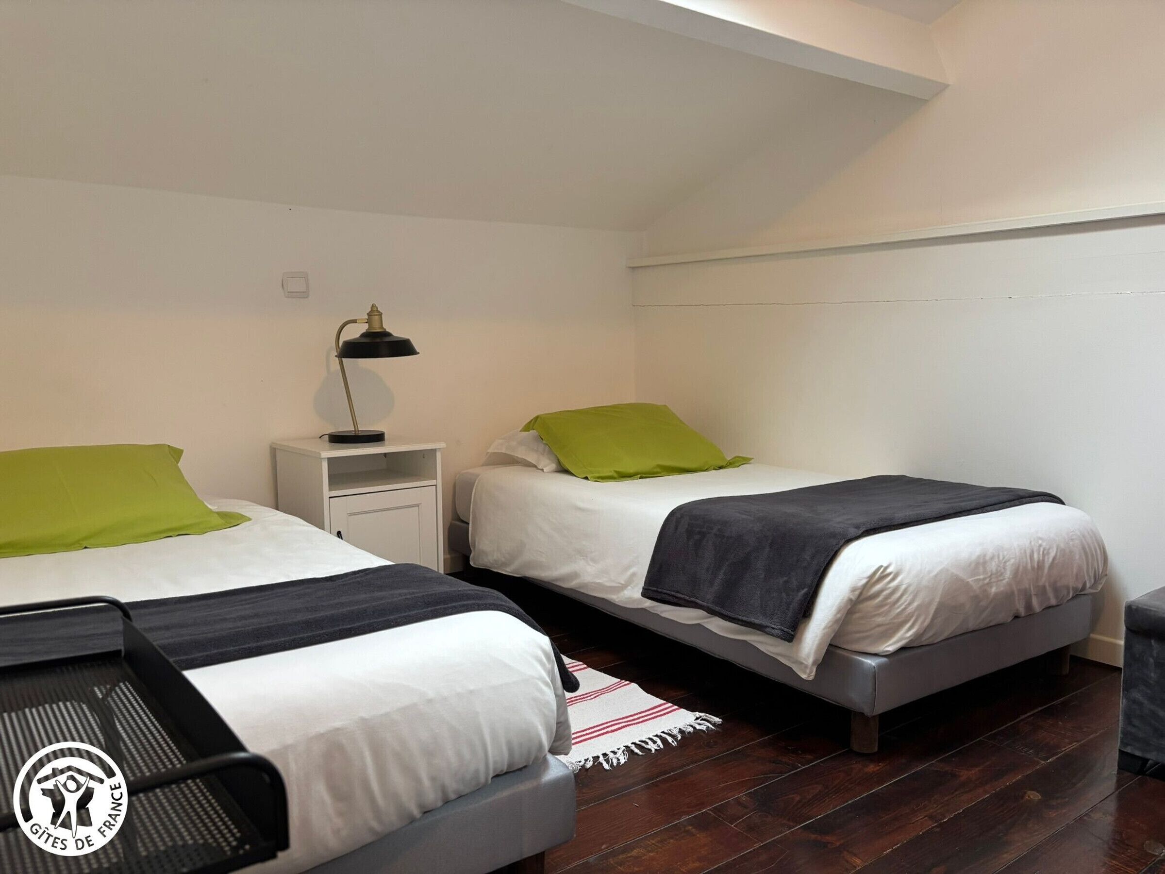 A bedroom with two beds, a nightstand with a lamp, and a wooden floor.