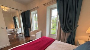 Hotellihuone, jossa on sänky, tuoli, peili ja ikkuna, jossa on verhot.