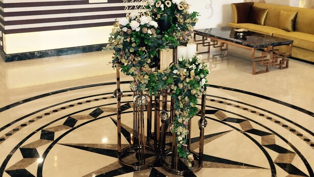 A lobby with a reception desk, a sofa, a coffee table, and a decorative plant arrangement. - Hotel Imperia Suites (Jalandhar)
