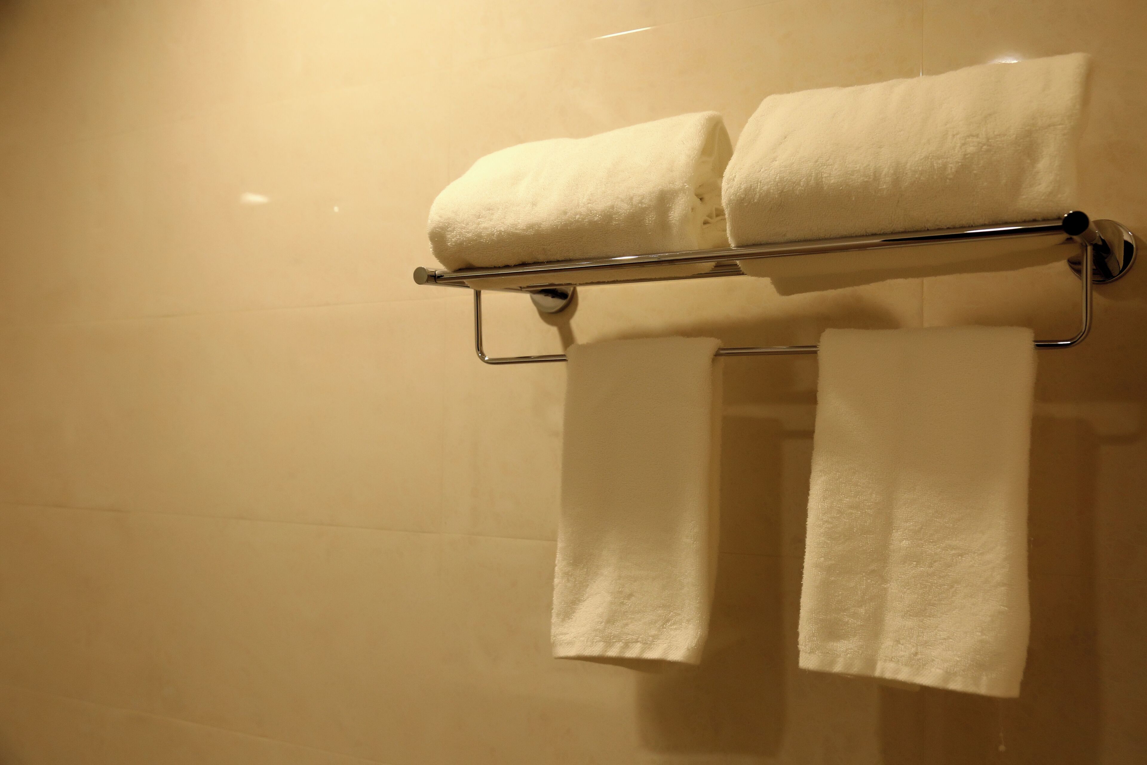 A bathroom with a towel rack holding two folded towels and a single towel hanging below.