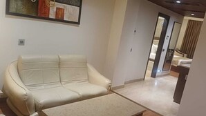 A hotel room with a sofa, a bed, a mirror, and a door leading to another room. - Hotel Imperia Suites (Jalandhar)