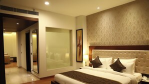 A hotel room with a large bed, a glass partition, a tufted headboard, and a nightstand with a lamp. - Hotel Imperia Suites (Jalandhar)