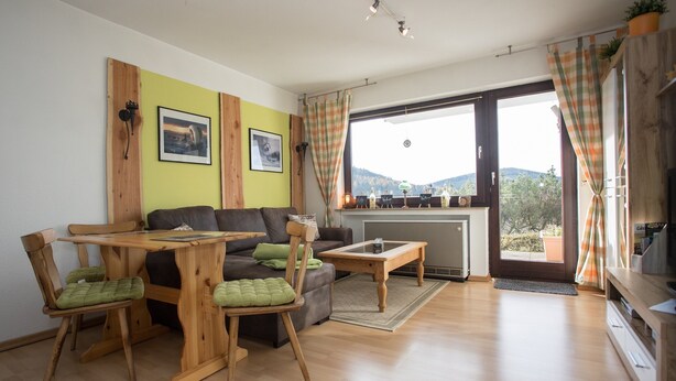 A cozy living room with a wooden dining table, two chairs, a sofa, and a television. - Kleine Wohnung Nahe Winterberg mit Terrasse (Winterberg)
