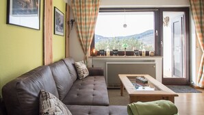 A living room with a sofa, a coffee table, and a view of the outdoors. - Kleine Wohnung Nahe Winterberg mit Terrasse (Winterberg)