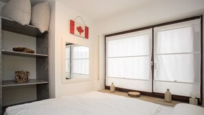 A bedroom with a bed, a wardrobe, a shelf with decorative items, and a window with curtains. - Kleine Wohnung Nahe Winterberg mit Terrasse (Winterberg)