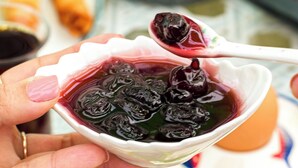 A person holding a bowl of dark-colored jelly with a spoon. - Anzede Konaklama Çeşme (Çesme)