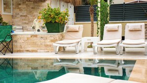 A poolside area with lounge chairs, a green plant, and a brick wall. - Anzede Konaklama Çeşme (Çesme)