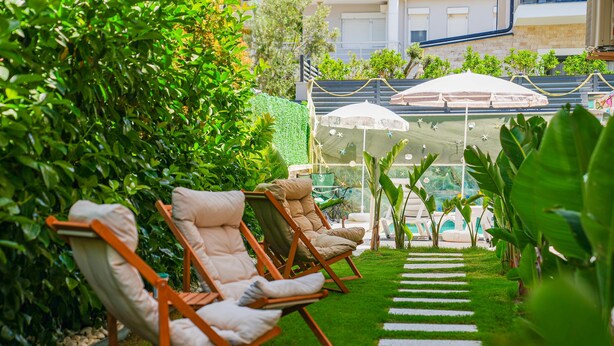 A row of lounge chairs with cushions, a grassy pathway, and a white umbrella structure in the background. - Anzede Konaklama Çeşme (Çesme)