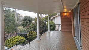 Ein überdachter Balkon mit Fliesenboden, weißen Säulen und einer Ziegelwand.