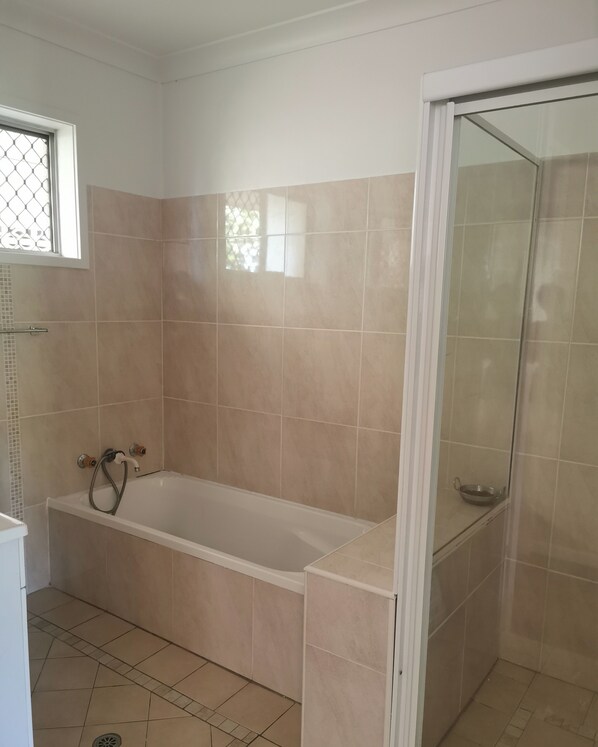 Un baño con bañera, cabina de ducha de cristal y azulejos color beige.
