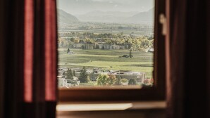 A window with curtains, revealing a view of a landscape with mountains and fields. - Appartements Elke (Lagundo)