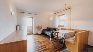A modern, well-lit room with a wooden desk, a sofa, and a small dining table. - Appartements Elke (Lagundo)
