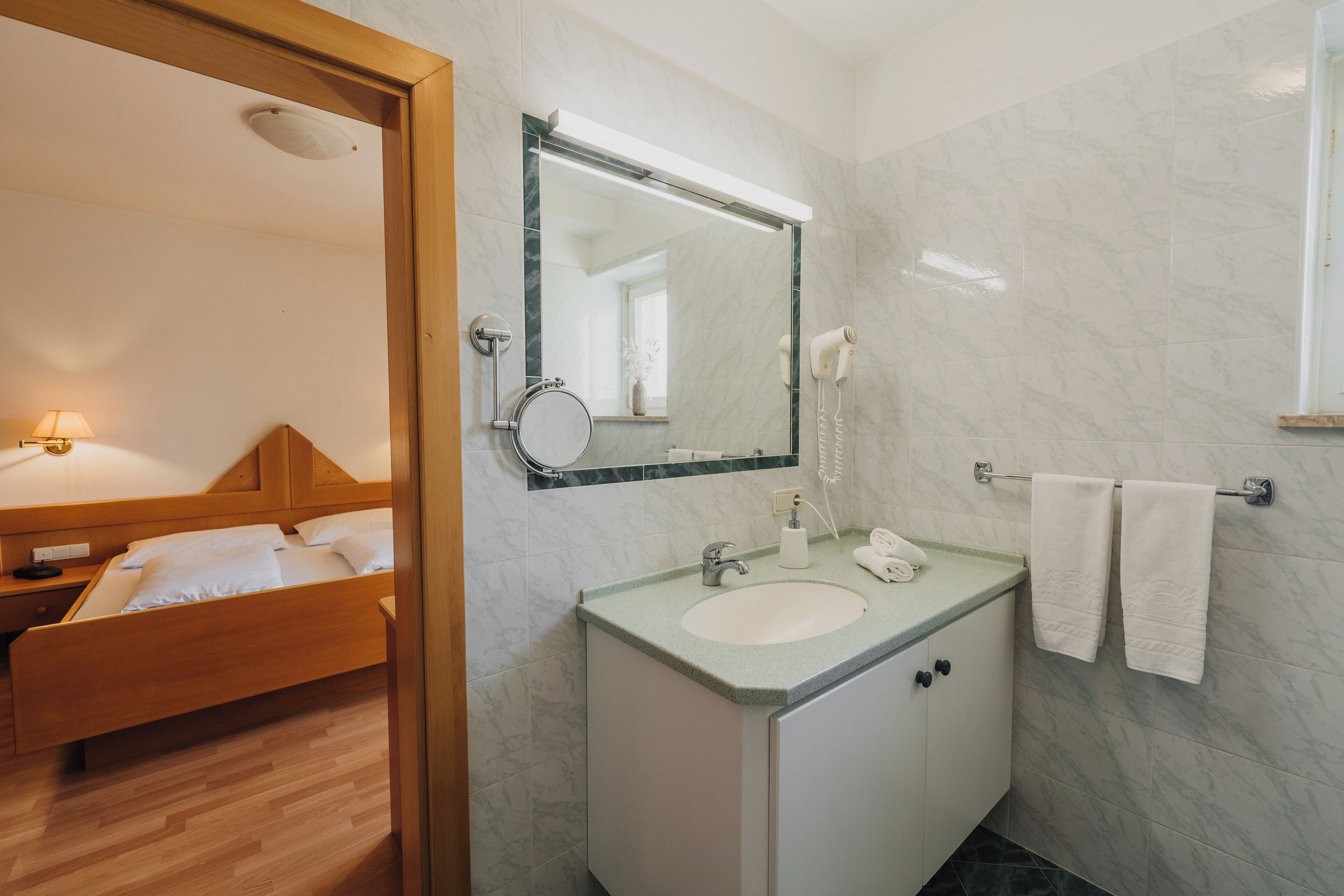 A hotel bathroom with a wooden bed, a sink with a mirror, and a towel rack.