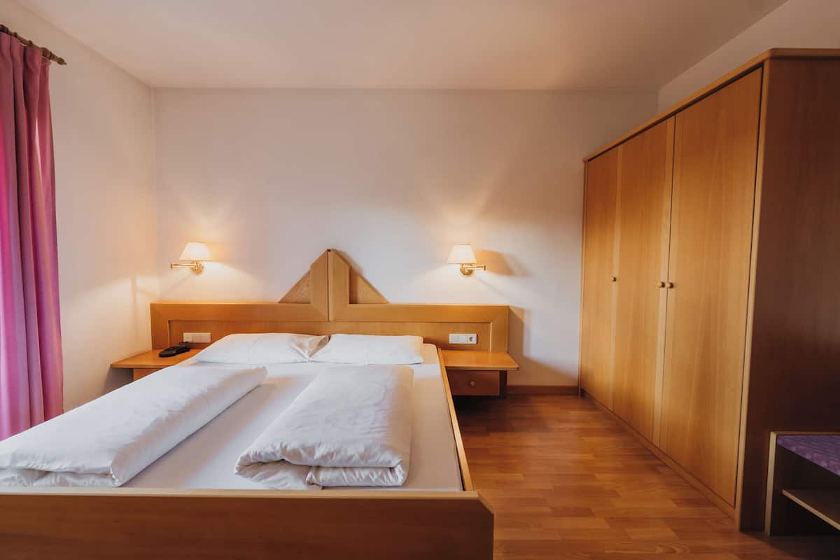 Una camera d'albergo con un letto in legno, due comodini, un armadio e una panca.