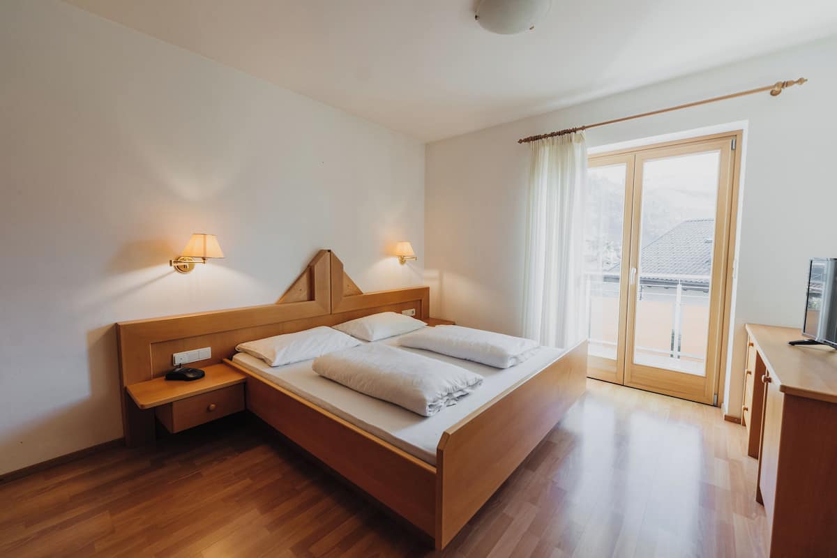 Un letto rifatto con cura, una testiera in legno, due comodini con lampade e vista all'esterno tramite una porta vetrata.