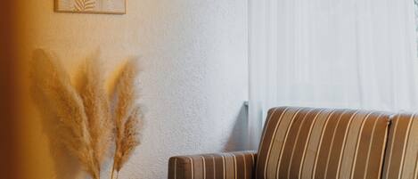 A living room with a striped sofa, a vase with pampas grass, and a framed picture on the wall.