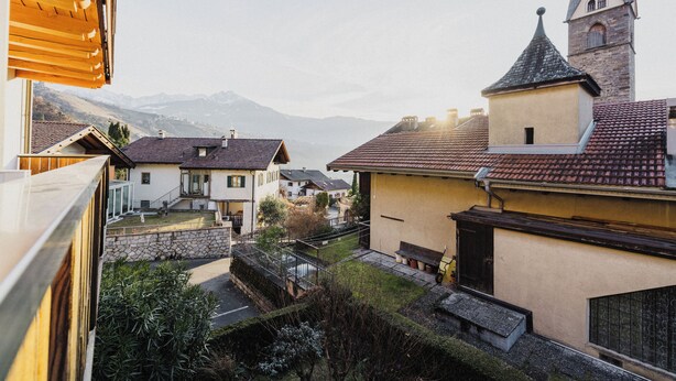 A residential area with houses, a stone wall, and a view of distant mountains. - Appartements Elke (Lagundo)