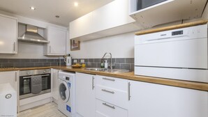 A modern kitchen with white cabinets, a stainless steel sink, a built-in oven, a washing machine, and a Zanussi refrigerator.