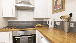 A modern kitchen with white cabinets, a stainless steel range hood, a wooden countertop, a kettle, and a bowl of croissants.