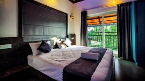 Habitación de hotel moderna con una cama grande, un cabecero oscuro y un balcón con vistas a zonas verdes.