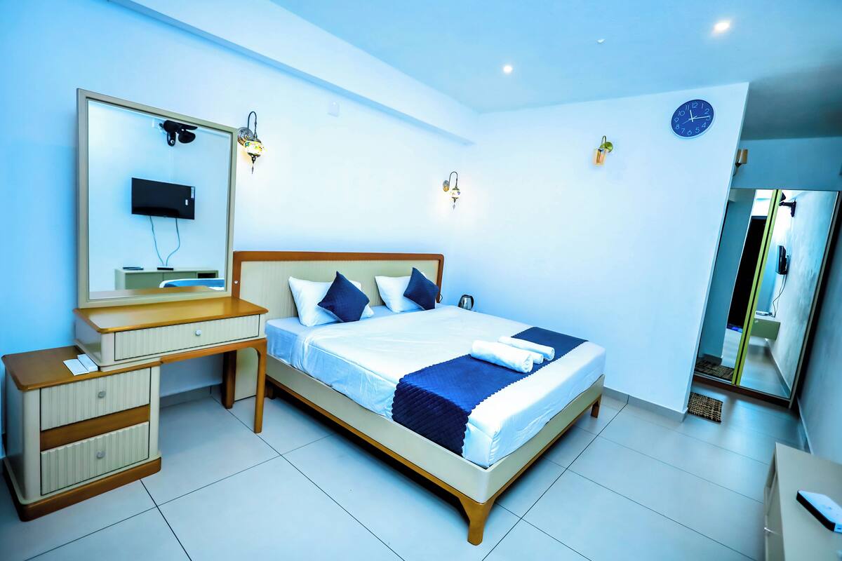 A modern bedroom with a bed, bedside table, dresser, and a large mirror.