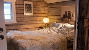 A cozy bedroom with a wooden log wall, a bed with floral bedding, a framed picture, and a lamp. - Cozy Cabin Retreat in Scenic Valley, E6 South of Trondheim (Midtre Gauldal)