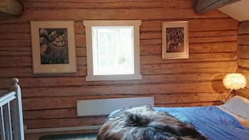 Cozy cabin bedroom with a bed, window, and framed pictures on the wall.