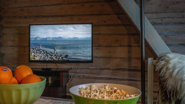 A wooden interior with a television displaying a scenic view, a bowl of popcorn, and oranges on a table. - Cozy Cabin Retreat in Scenic Valley, E6 South of Trondheim (Midtre Gauldal)