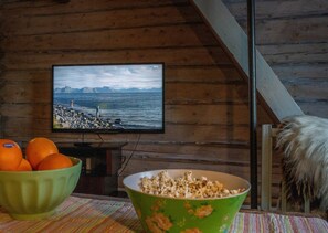A wooden interior with a television displaying a scenic view, a bowl of popcorn, and oranges on a table. - Cozy Cabin Retreat in Scenic Valley, E6 South of Trondheim (Midtre Gauldal)