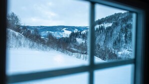 A snowy landscape through a window with a view of snow-covered hills and trees. - Cozy Cabin Retreat in Scenic Valley, E6 South of Trondheim (Midtre Gauldal)