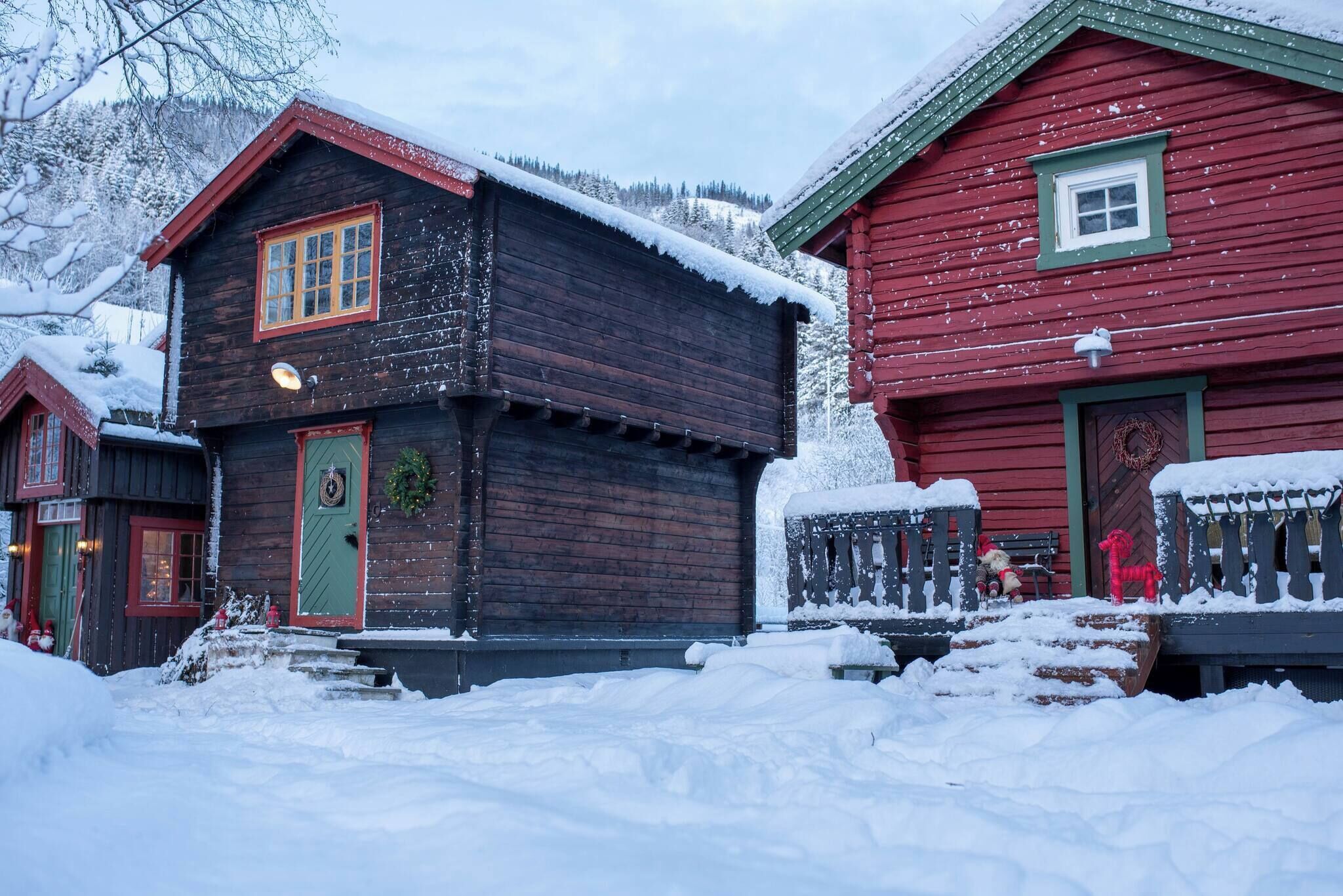 A wooden cabin with a red door and a green window, surrounded by snow.