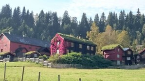 A rural setting with a red barn, a house with a green roof, and a forest in the background. - Cozy Cabin Retreat in Scenic Valley, E6 South of Trondheim (Midtre Gauldal)