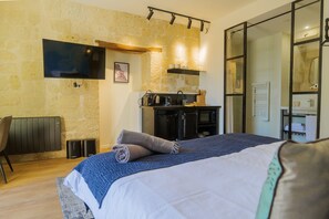 A bedroom with a bed, a desk, a TV, a radiator, and a kitchenette. - When heritage, art and well-being meet (CANDES SAINT MARTIN)