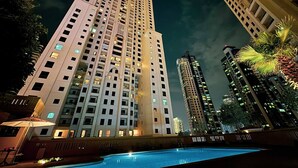 Um hotel moderno com vários andares, uma piscina em primeiro plano e edifícios altos ao redor.